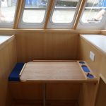 5. A mess table and bench seats are installed on the port side of the wheelhouse.