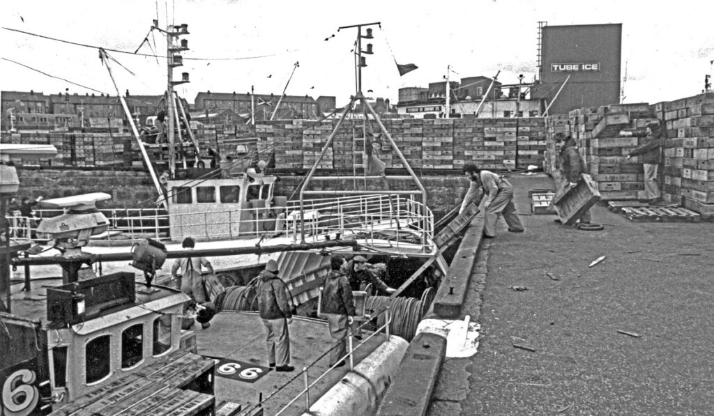 The crew of the Buckie seine-netter Hopecrest BCK 166 are taking traditional wooden fishboxes aboard at the end of a trip.